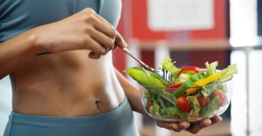 Effective Ways To Keep Your Stomach Healthy Close up of a sport woman with her sexy belly, she holding a bowl of fresh healthy food